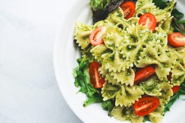 pesto pasta with sliced Pesto pasta with sliced tomatoes served on white ceramic plate