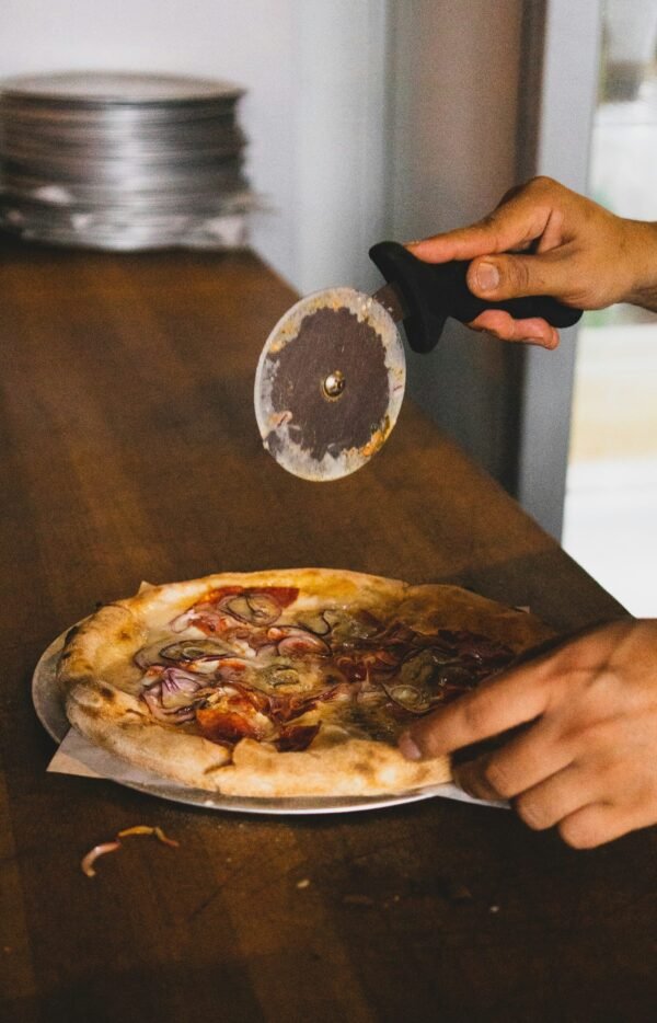 person holding pizza slicer over pizza